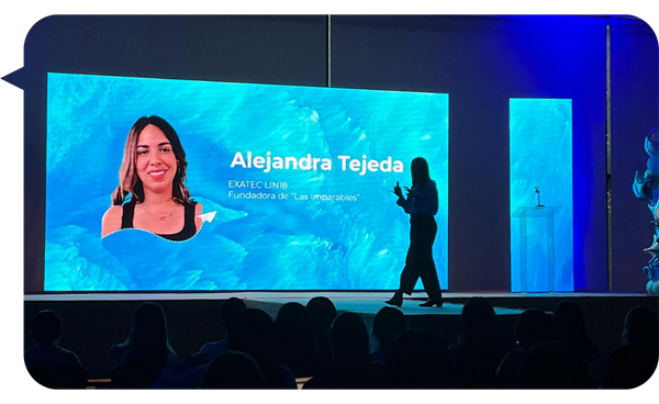 Alejandra Tejeda en el escenario, presentando en una conferencia con su nombre y foto en una pantalla grande detrás de ella.