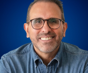 Sergio Talavera, destacado comunicador y consultor en liderazgo y desarrollo organizacional, sonriendo con camisa de mezclilla y gafas.