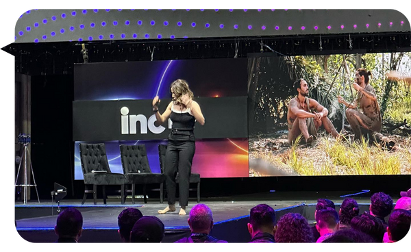 Fernanda Pérez Alarcón en el escenario de INC MTY, compartiendo su experiencia en supervivencia con una imagen proyectada de su participación en Supervivencia al Desnudo Latinoamérica.