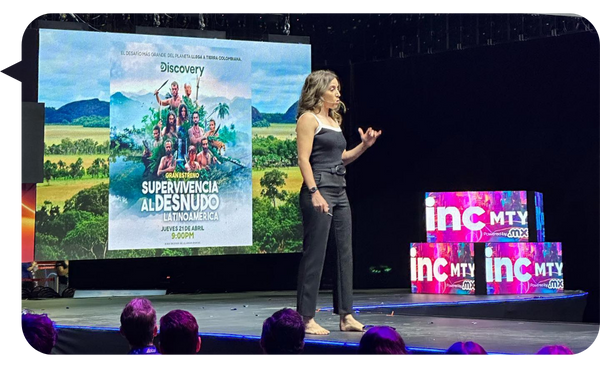 Fernanda Pérez Alarcón en el escenario de INC MTY, compartiendo su experiencia en Supervivencia al Desnudo Latinoamérica con una imagen del programa proyectada detrás de ella.