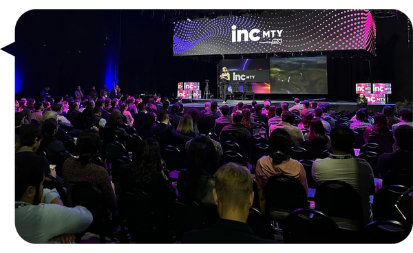 Fernanda Pérez Alarcón impartiendo una conferencia en INC MTY ante una audiencia numerosa y atenta, con un escenario iluminado y una gran pantalla de fondo.