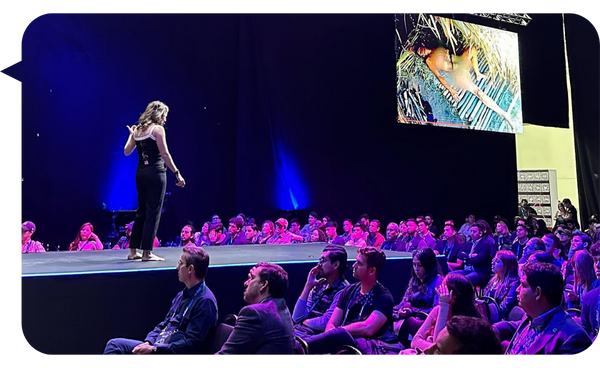 Fernanda Pérez Alarcón dando una conferencia en un gran escenario ante una audiencia atenta, con una imagen de su experiencia en supervivencia proyectada en la pantalla.