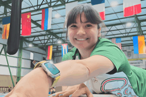 Alexa Moreno sonríe mientras entrena en un gimnasio internacional con banderas al fondo, promoviendo el deporte juvenil en la Believe Cup 2025.